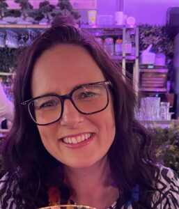A woman with long dark hair and glasses smiles at the camera